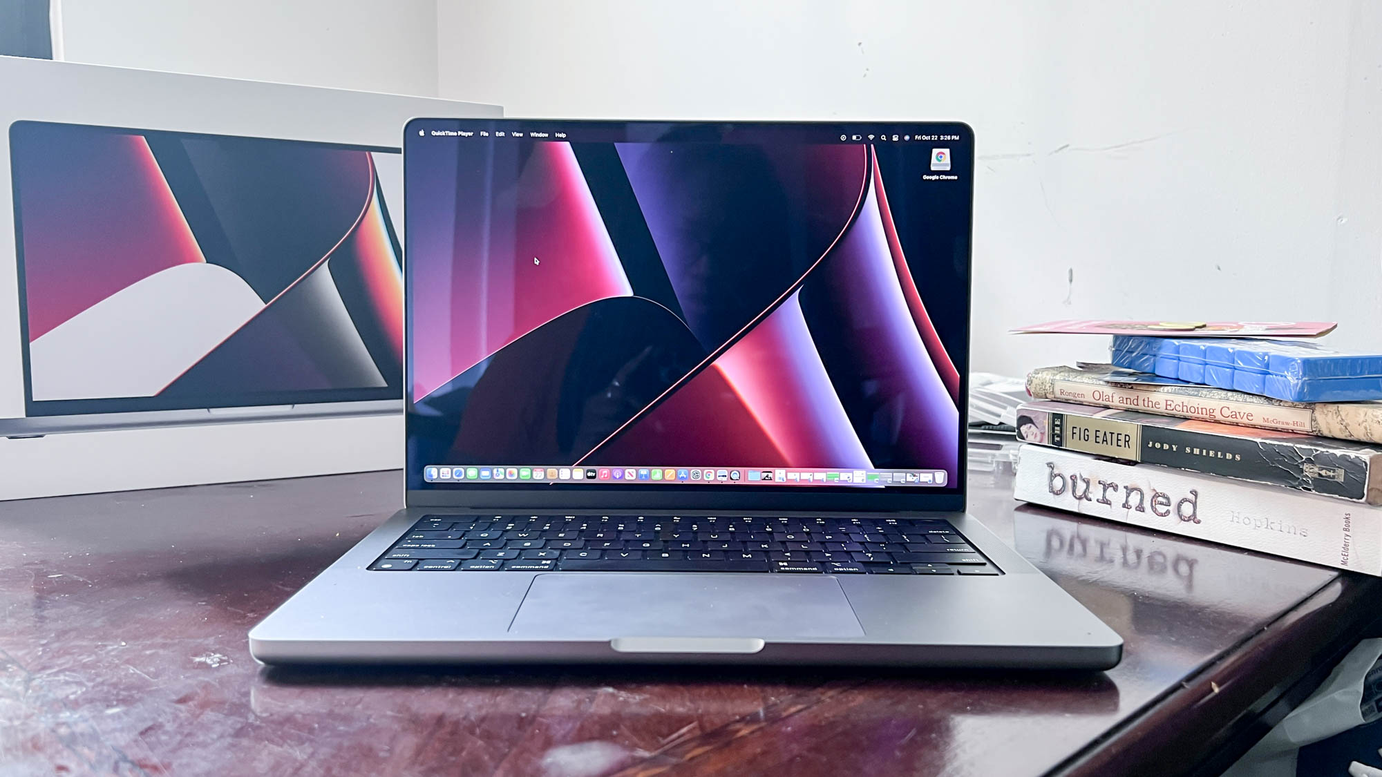 Apple MacBook Pro on a wooden desk next too books and retail packaging