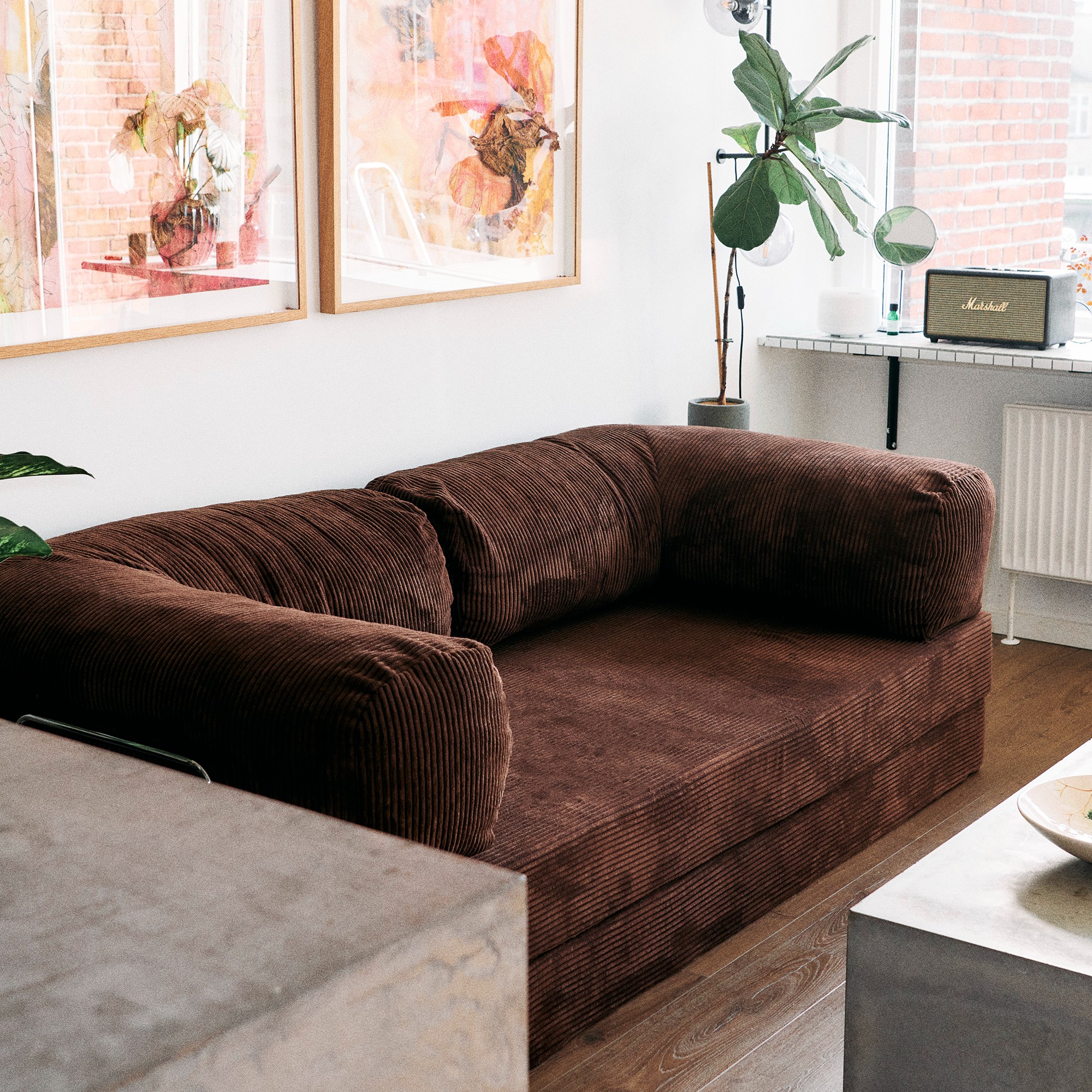 The brown Teddy sofa by OMHU in a living room with abstract artwork hung above it and a Marshall radio on the windowsill to the side