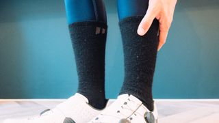 A man wears a set of white cycling shoes, black fluffy socks, and blue tights against a blue background