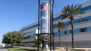 a cylindrical blue rocket propellant tank stands outside an office building on a sunny day