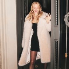 Model wearing a white fur coat and LBD sold at Fenwick walking through a doorway