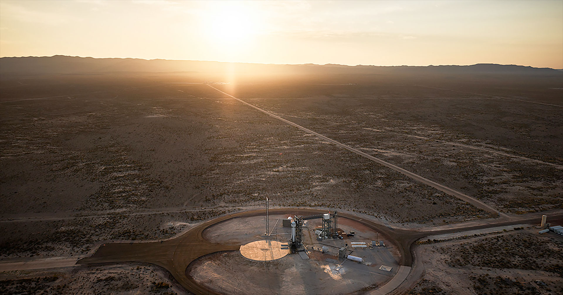 aerial view of a rocket standing on its launch pad as the sun rises over the horizon.