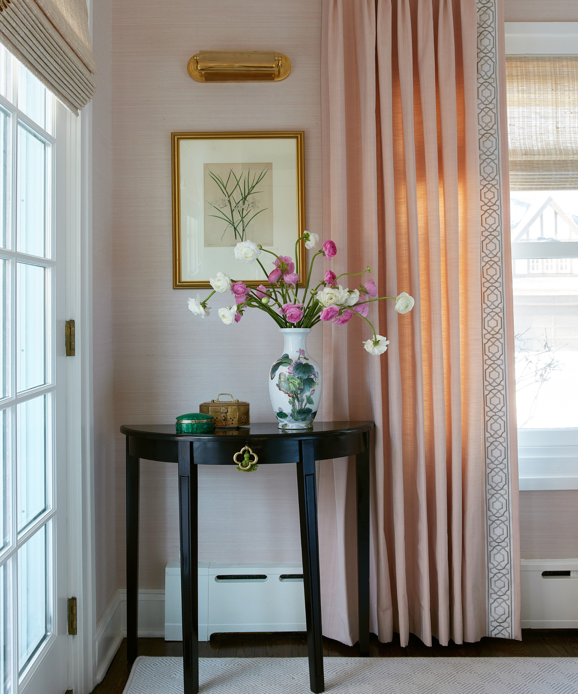 a corner in a room with a black painted demilune table holding some trinkets and a vase with flowers