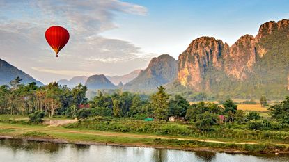 A red hot air ballon hovers over a jungle scene in Laos