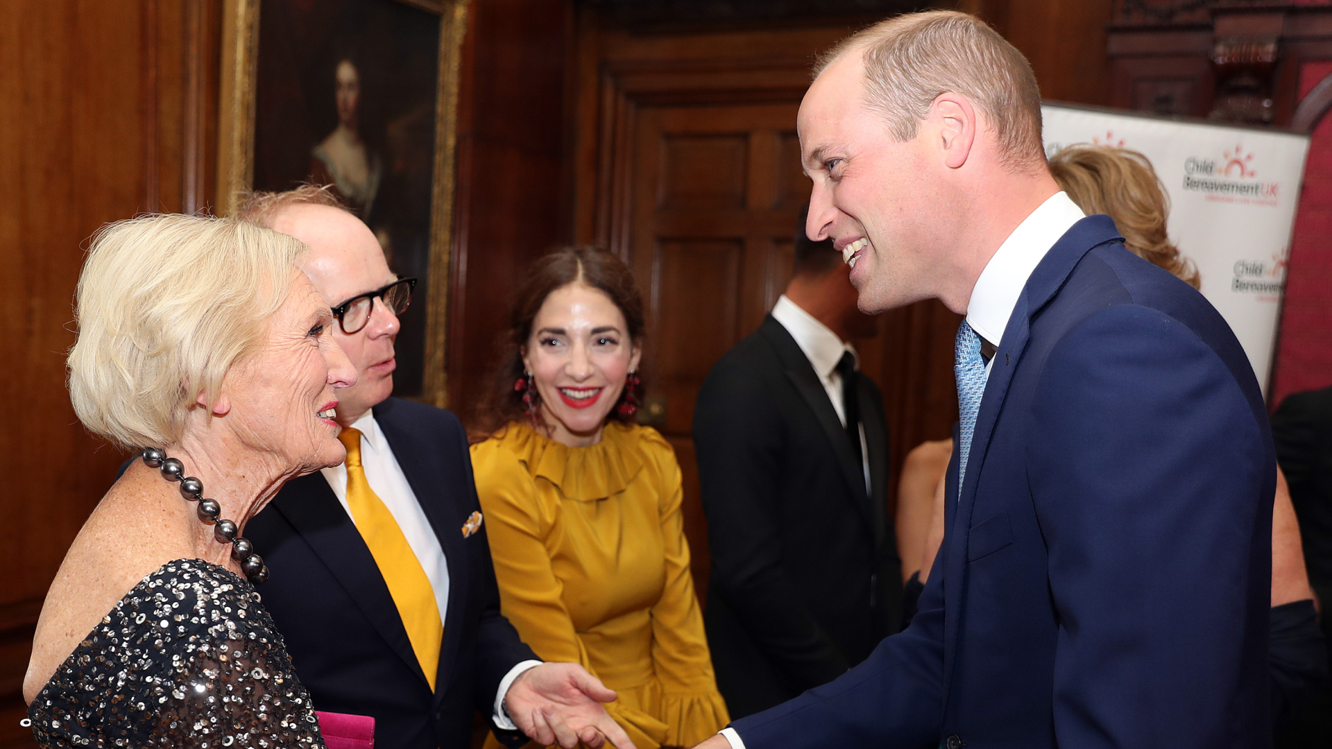 Prince William wearing a blue suit shaking hands with Mary Berry