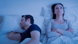 A woman awake in bed at night while her partner sleeps