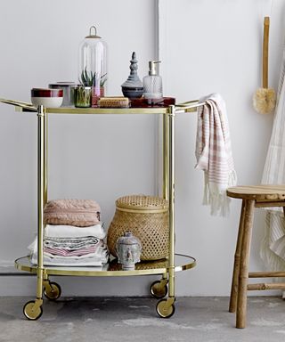 Brass drinks trolley styled with towels, toiletries and glass and ceramic vessels.