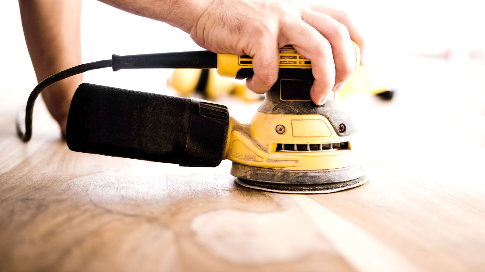 Hand holding yellow and black orbital sander on large wooden surface