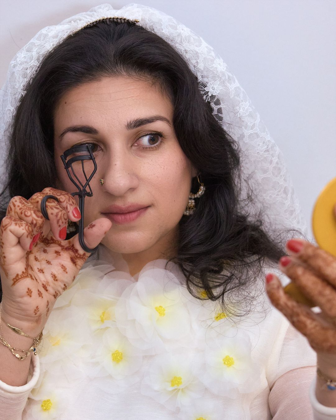 Kirin Bhatty wearing a wedding outfit and curling her lashes.