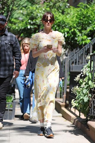 Dakota Johnson walking in New York City wearing a floral midi Dôen dress, Nike sneakers, and cat-eye sunglasses.