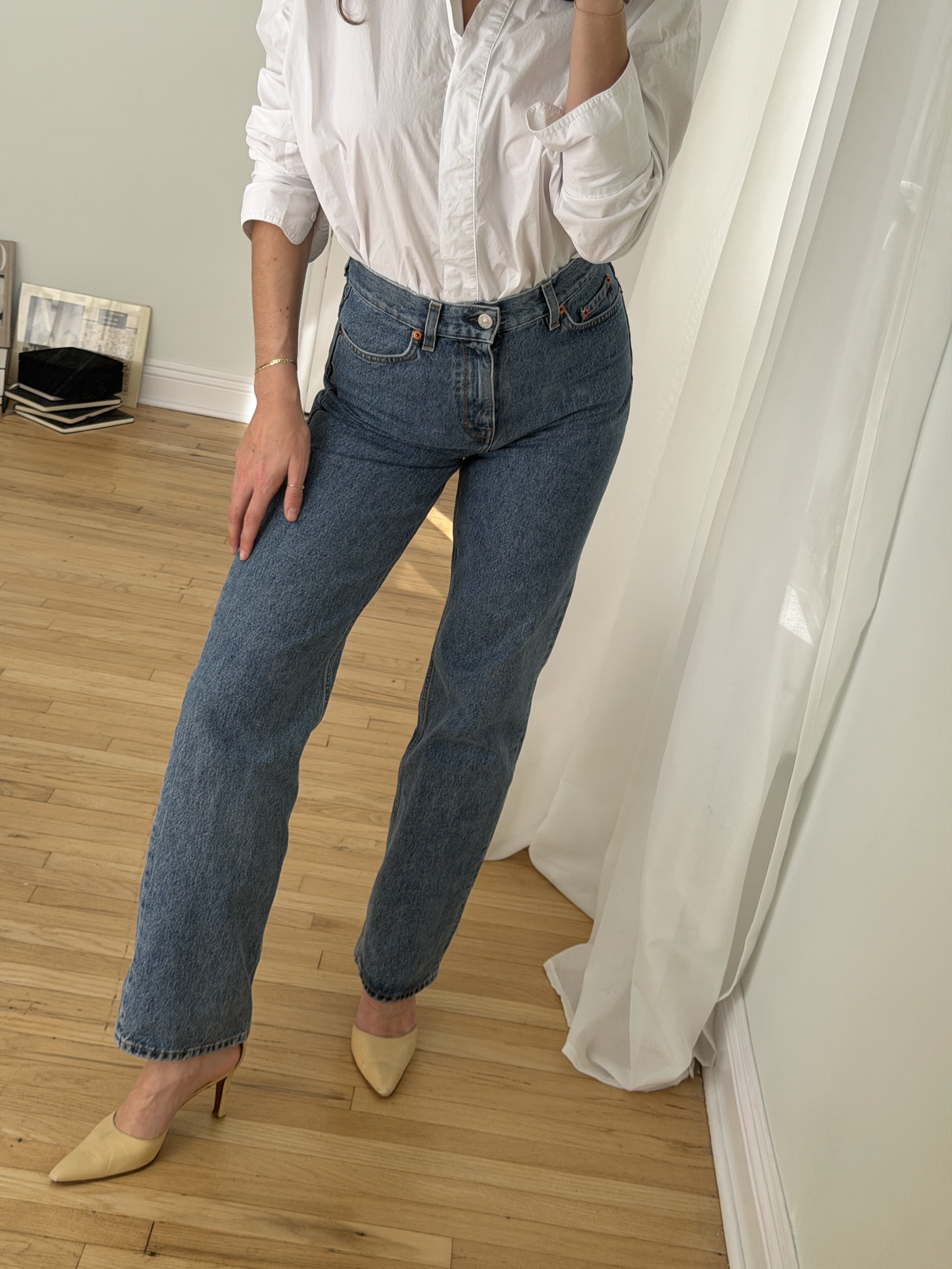 Kathryn Zahorak posing in mirror wearing white button-down shirt, jeans, and heels 