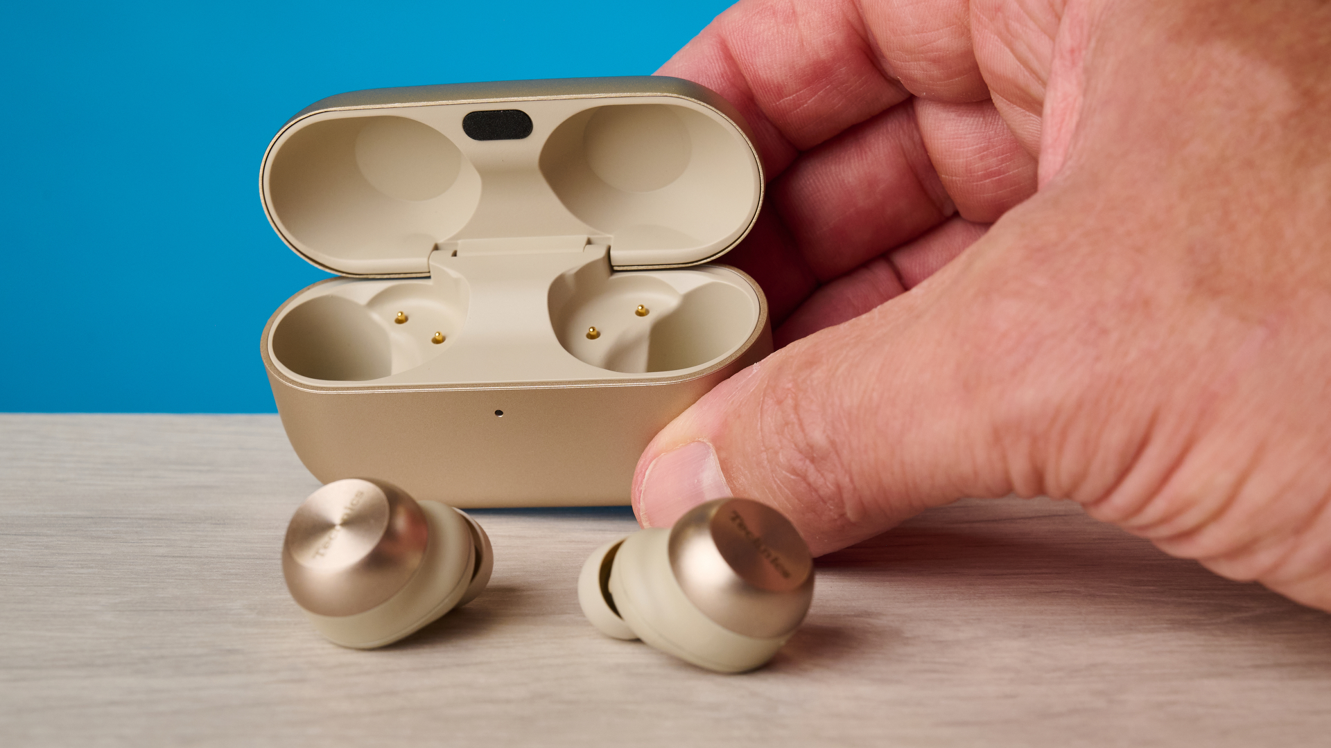 the technics az100 earbuds in champagne photographed against a blue tom's guide background