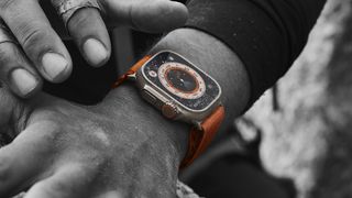 En svartvit bild på en Apple Watch Ultra runt en mans handled, som lyser upp i en orange färg.