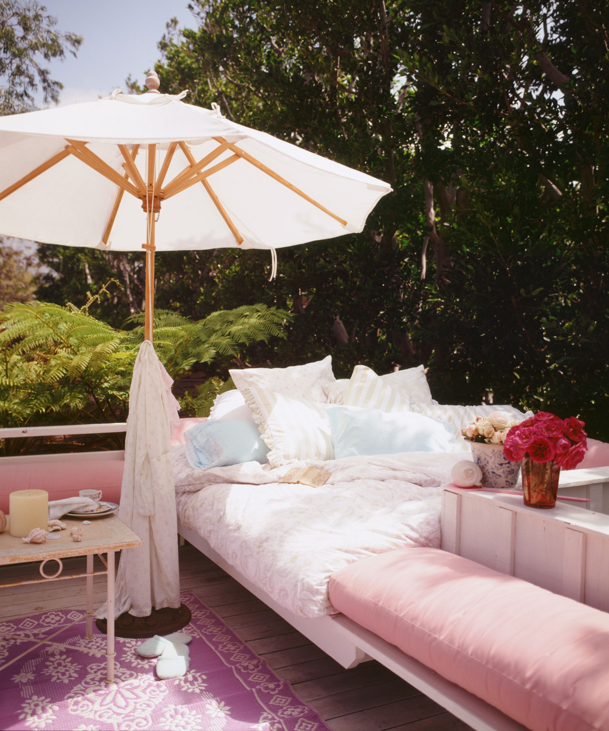 Outdoor bed and seating area with parasol in pink and white scheme
