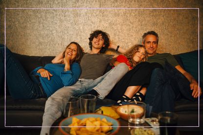 A family of four sitting together on a sofa and watching TV
