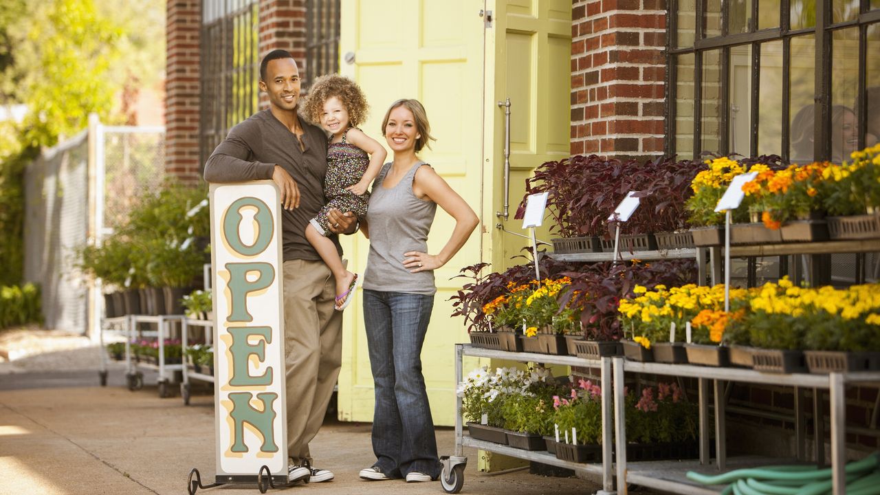 Business owners who are parents stand outside their florist with their young girl.