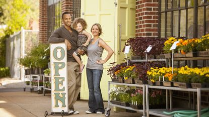 Business owners who are parents stand outside their florist with their young girl.