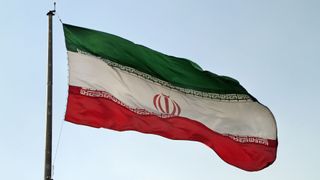 The Iranian flag flying against a cloudy, blue sky