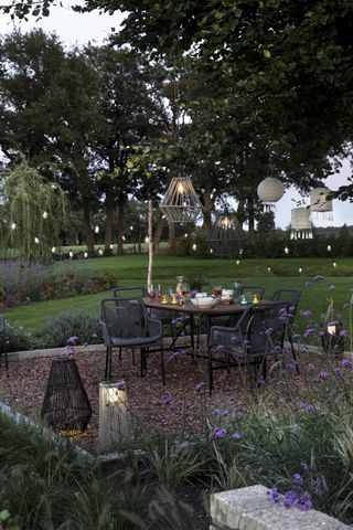 A gravel patio with a dining table and chairs and string lights