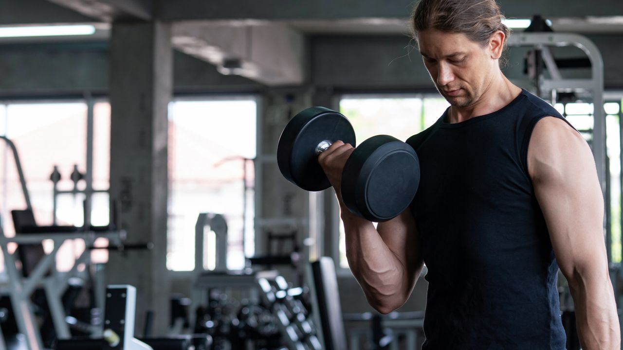 A man performing bicep curls with dumbbells, as part of his full-body workout