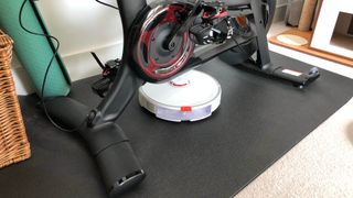 The Roborock S7 under a Peloton Bike+ with the power cable pulled out of the way