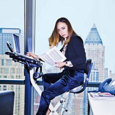 Woman in business clothing on an exercise bike.