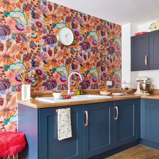 Kitchen area with blue units and pink floral wallpaper