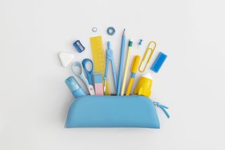 A blue pencil case with contents on show, including a glue stick, scissors, ruler, compass, paperclip, and more.