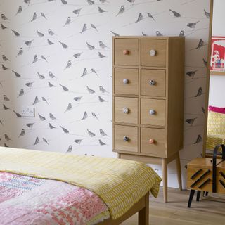 bedroom with white bird designed wallpaper wooden drawer shelve and wooden floor
