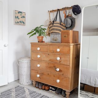Wooden chest of drawers with white knobs in a white bedroom