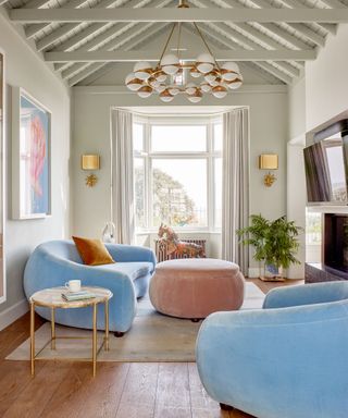 Minimalist gray/beige living room with pastel furniture including a sky blue sofa, pink footstall, two gold lamps and rug on wooden floors