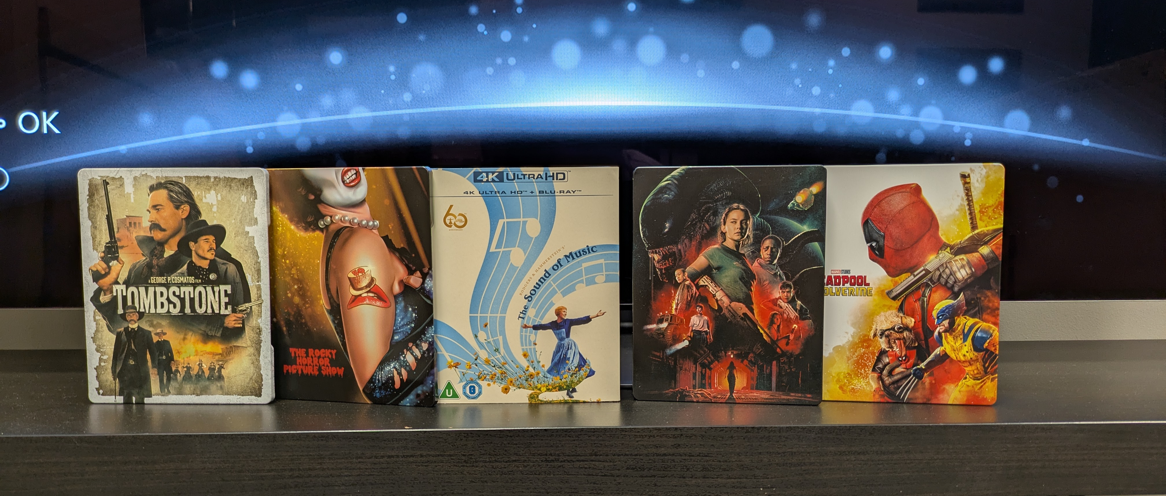 4K Blu-ray collection hero image with Tombstone, Sound of Music, Rocky Horror, Alien: Romulus and Deadpool and Wolverine 4K cases on dark bench 