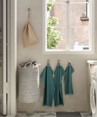 A laundry room with large window, washing machine, and laundry accessories (including green towels, and laundry bags on wall hooks)