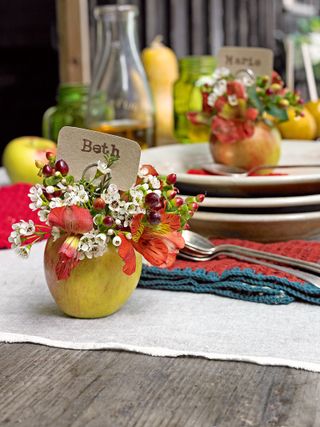 A table laid with plates and cutlery, and apples hollowed out for use as vases filled with autumn flowers and berries, and place names