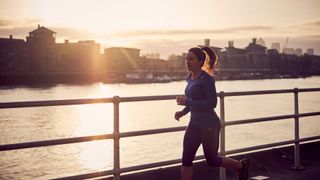 Woman in activewear running alongside river path at sunset with determined look, after learning how to prevent a hangover