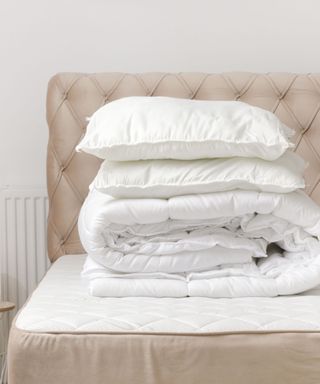 A white folded duvet on top of a beige upholstered bed frame with a white wall behind it