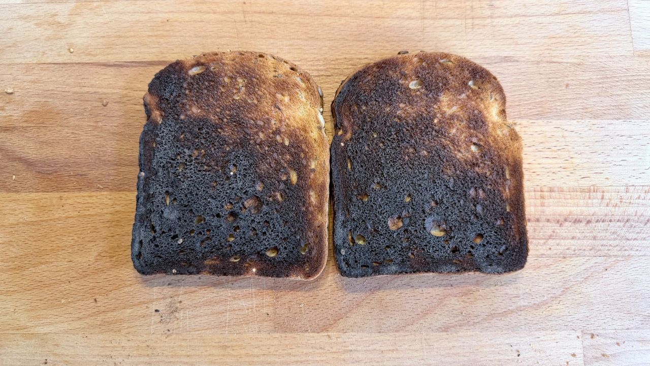Two slices of burned toast on a wooden board after being cooked in the KitchenAid Pro Line toaster