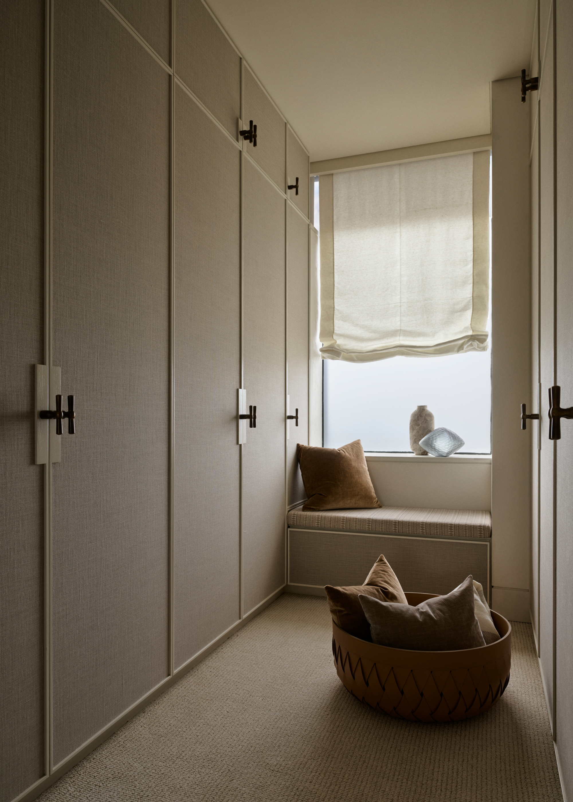 A neutral minimalist linen closet with a bay window and a basket with pillows