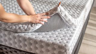 A woman pulls up the corner of a Layla Mattress Topper to show how thick it is