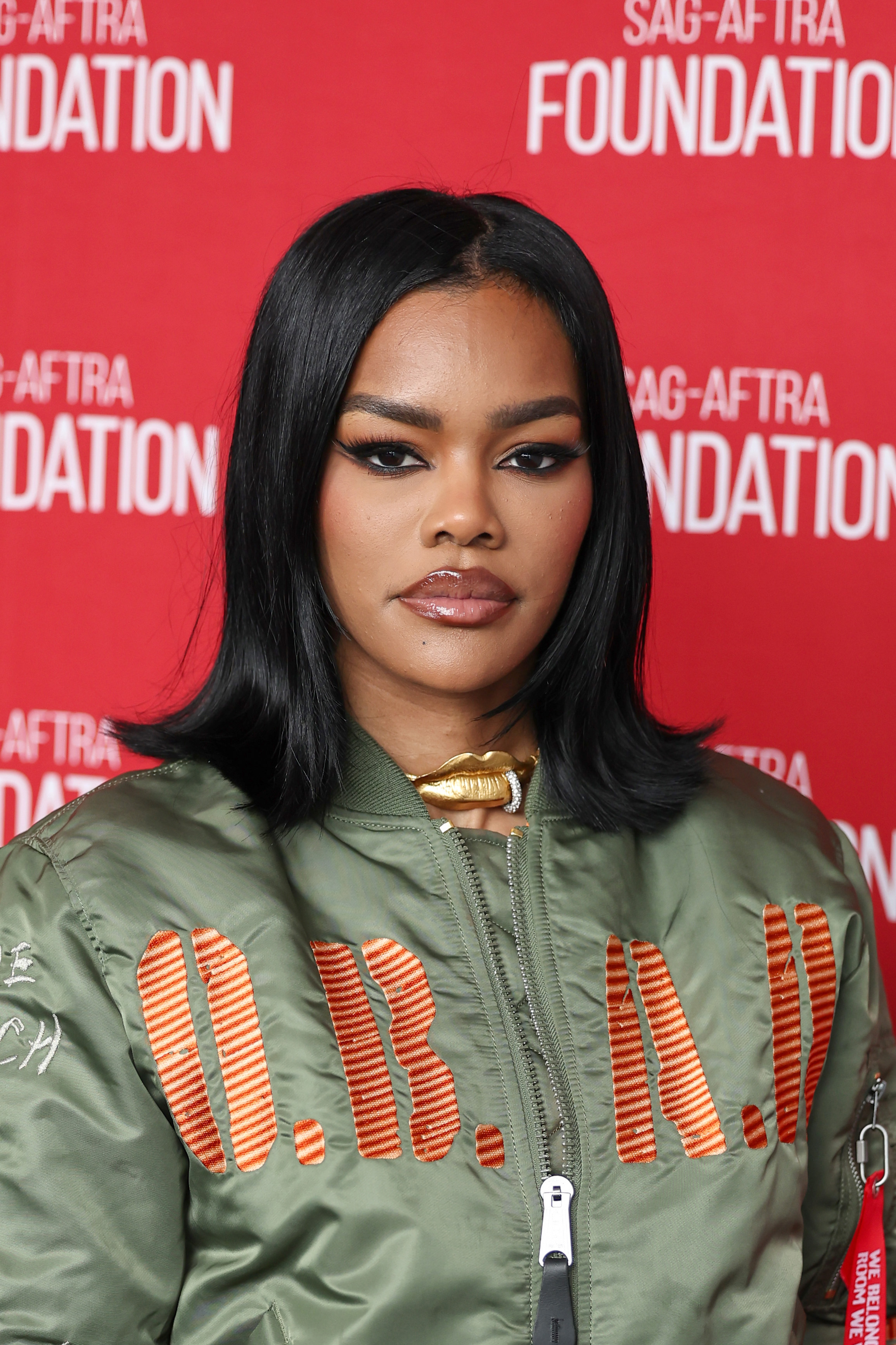 a black woman with dark hair posing in front of a red backdrop