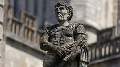 A close up of a gray statue of a man wearing a cloth toga and laurel crown.