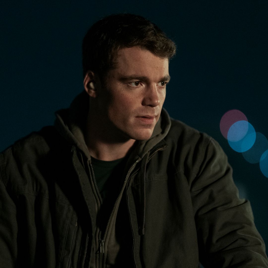 gabriel basso as peter sutherland wearing a jacket outside at nighttime in a still from the night agent season 2