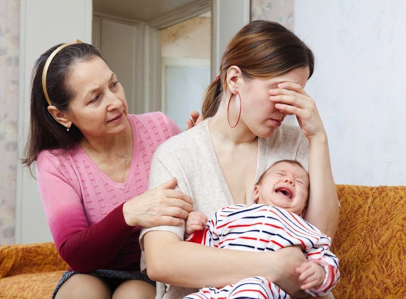 A woman cries while holding a baby, while an older woman looks on and tries to offer comfort.