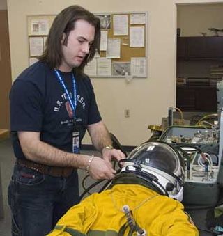 NASA life support engineering technician Joshua Graham performs a pre-flight inspection of a pressure suit.