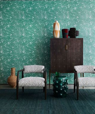 Living room picture showing deep green wallpaper with patterned chairs in front.