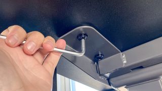 An allen wrench loosening a bolt under a standing desk