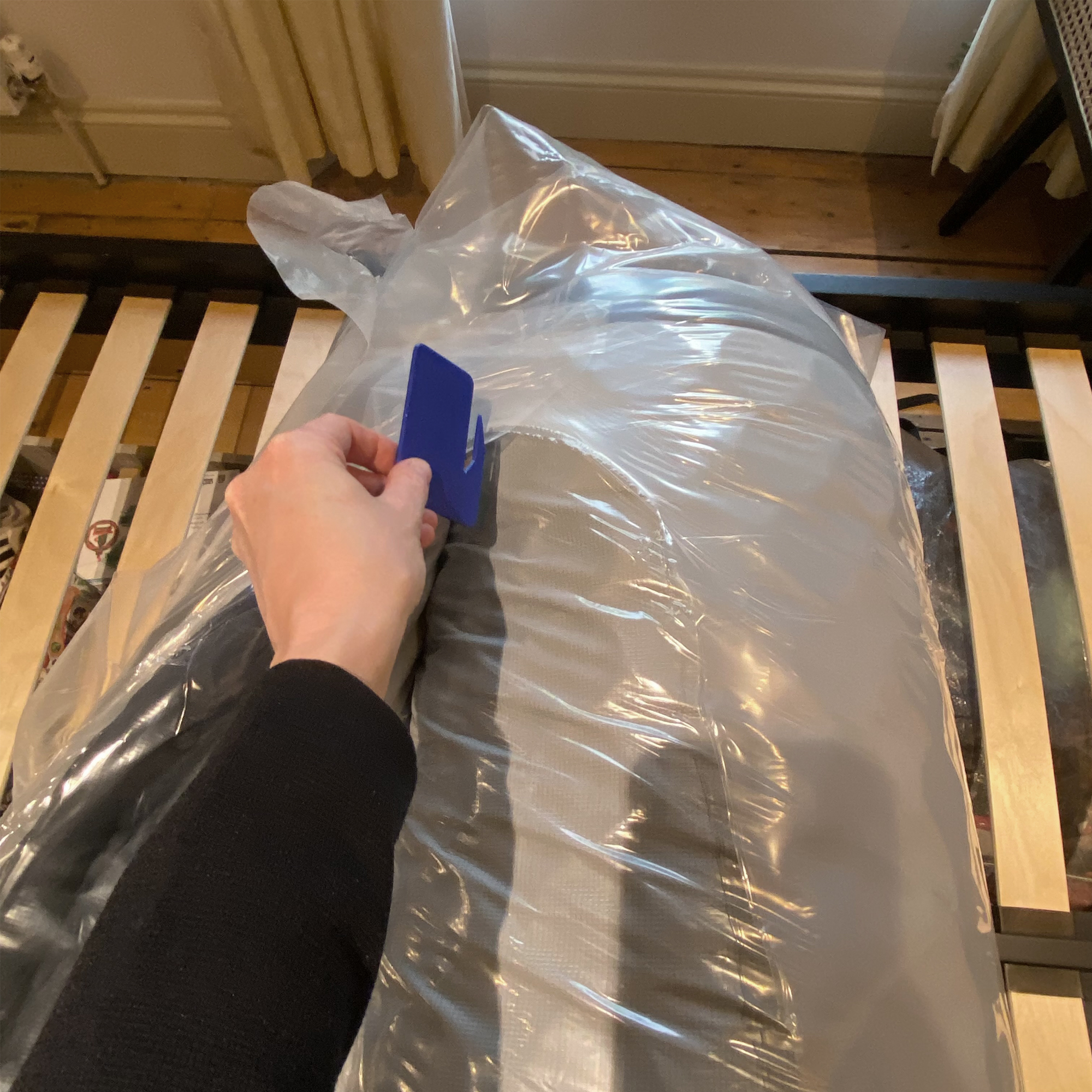 A woman's hand cutting open a rolled mattress with a blue plastic cutting tool