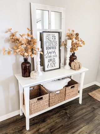 Seasonal console in white entryway decorate with gourds foliage and fall inspired frames