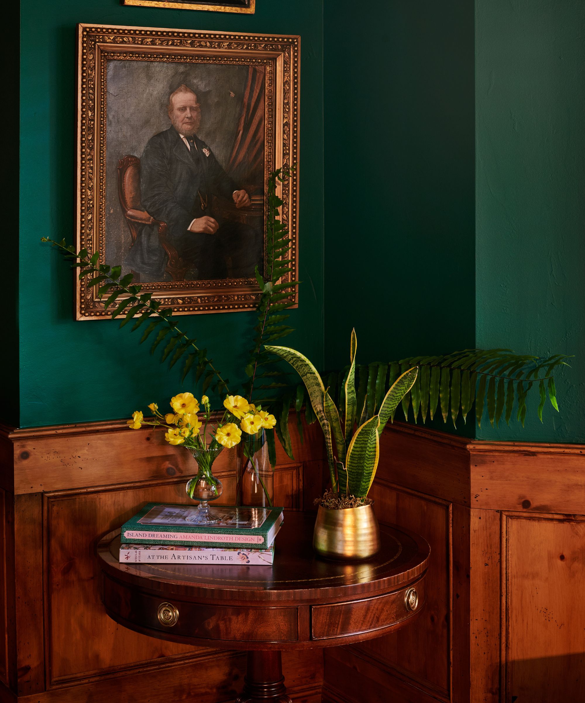 A dark green room with wood paneling, a pedestal table, and gilded frames