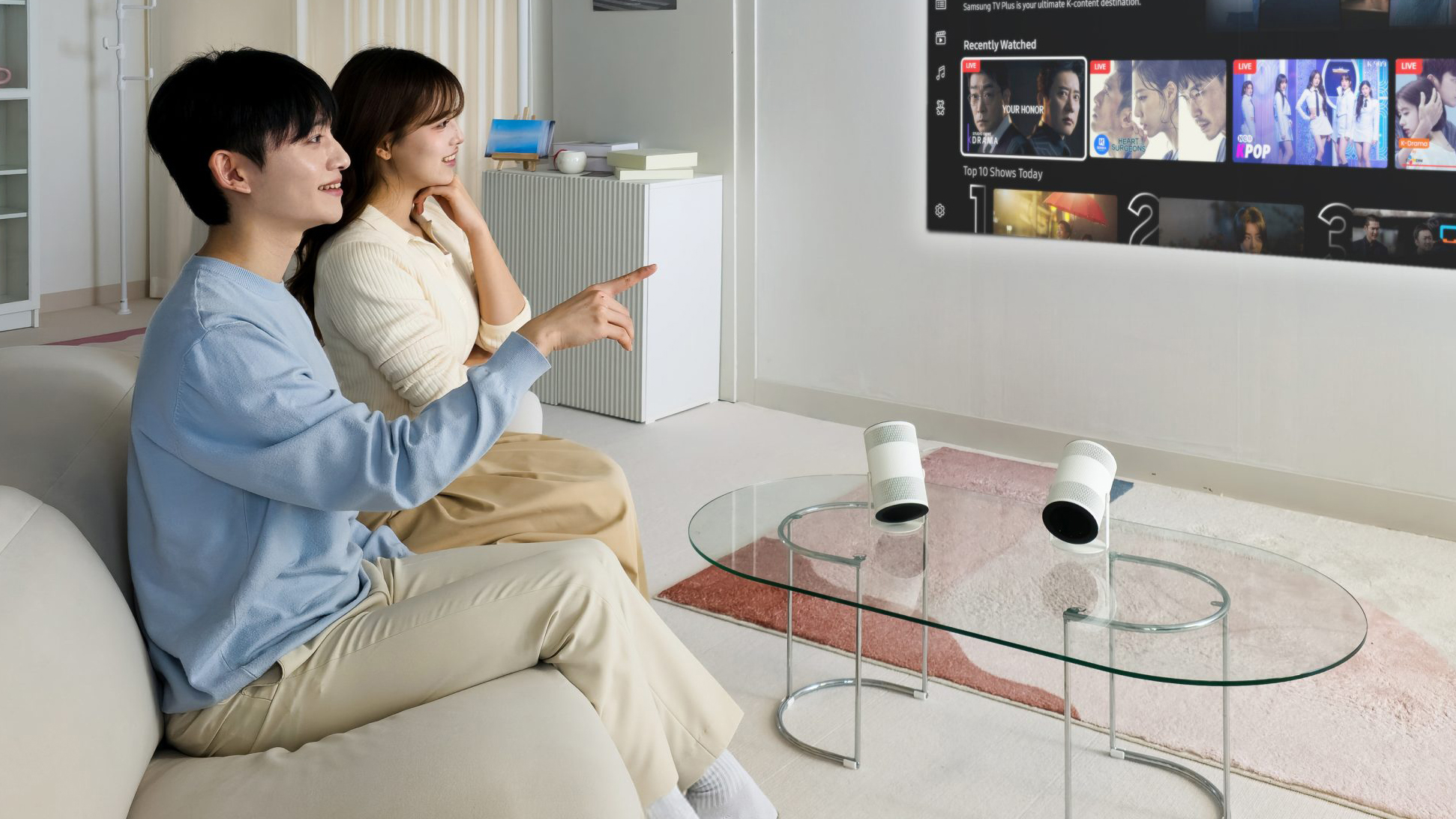 Samsung The Freestyle+ on table, projecting smart TV software on the wall while two people watch it
